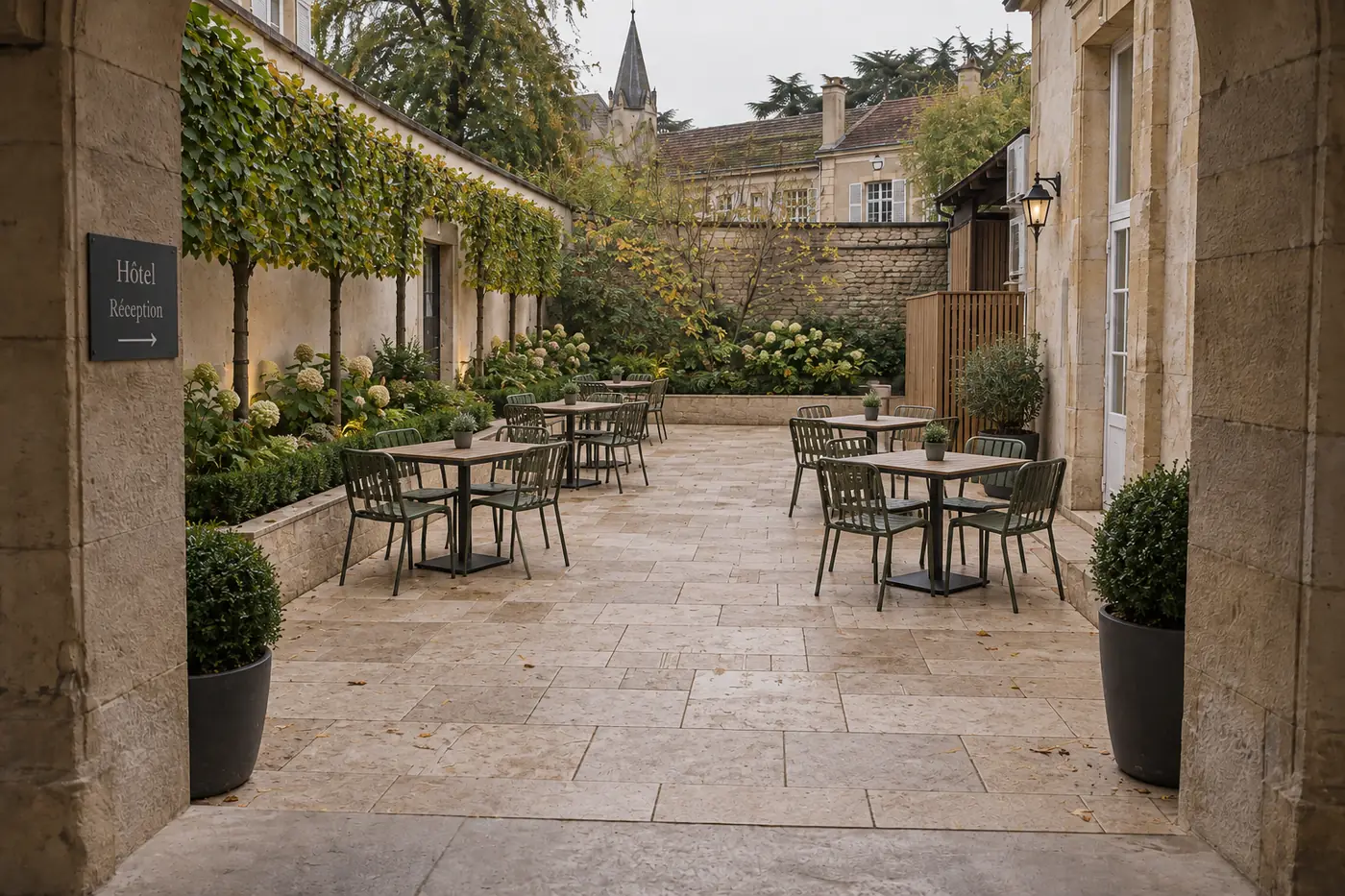 La cour de l'hôtel terminée : dallage en pierre claire, charmes palissés, tables et chaises